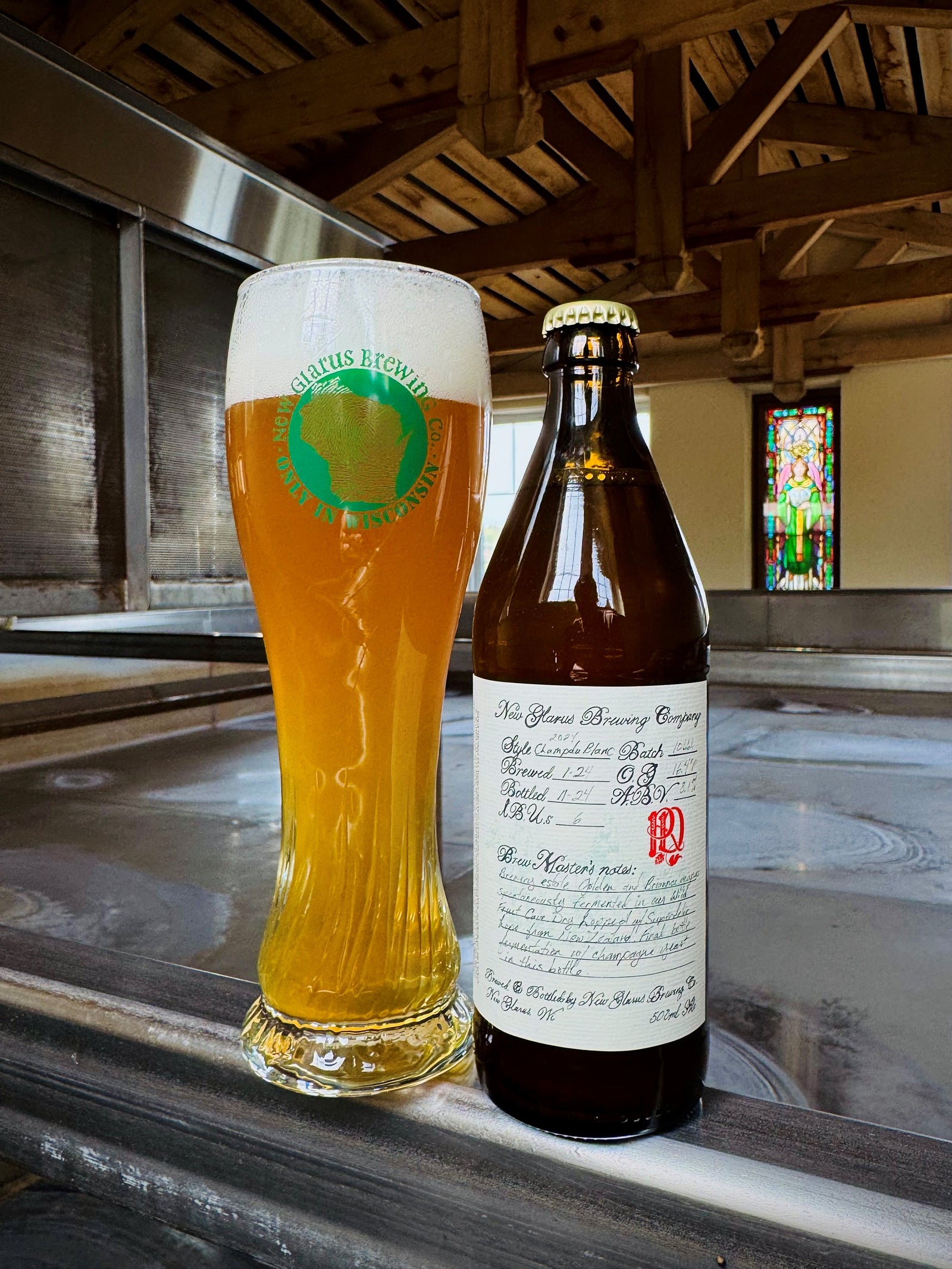 Beer bottle and glass on a metal surface in a brewery.