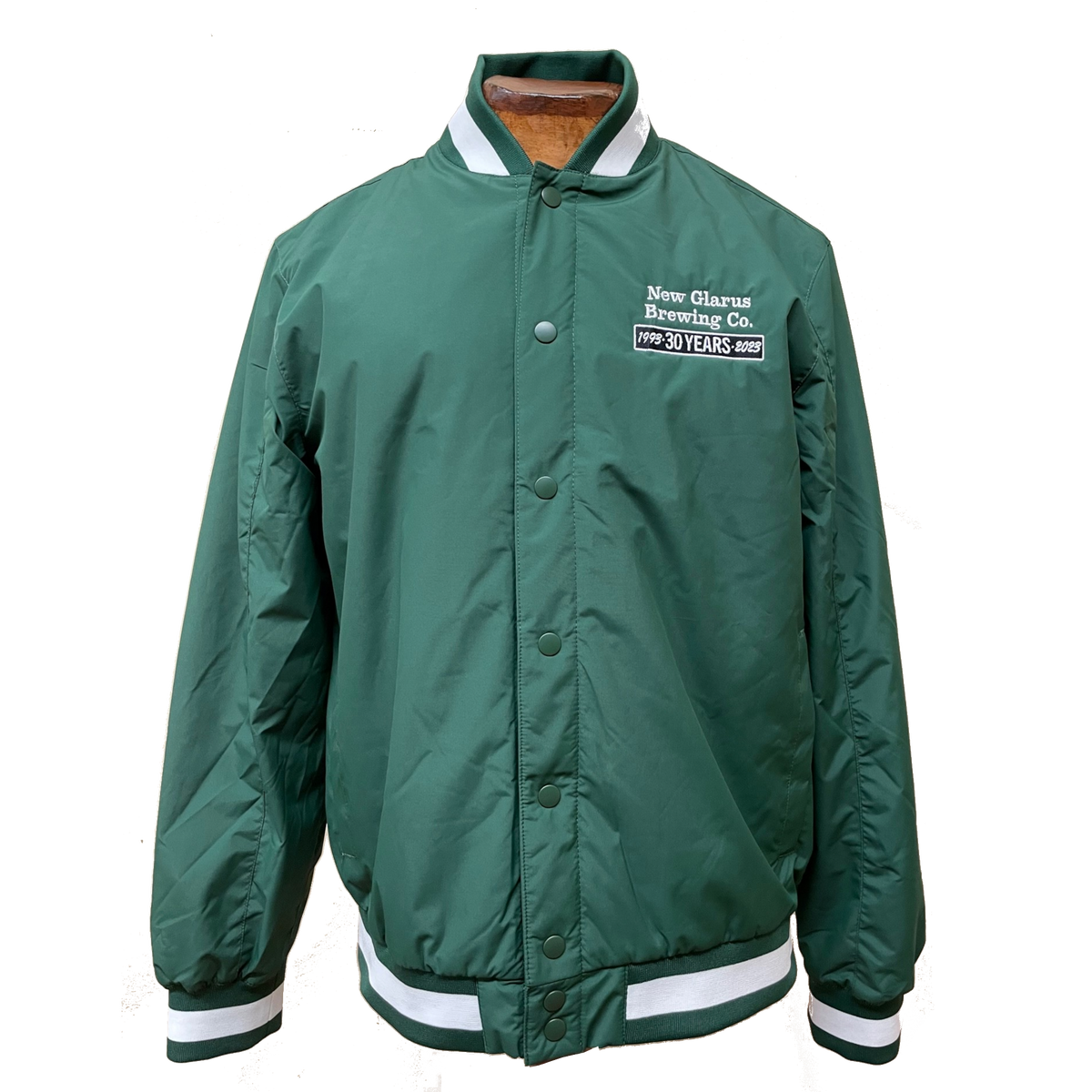 Snap button down green varsity jacket, with white striping along wrist, collar, and waist. Block white and black stitching on left side. Celebrating 30 years.