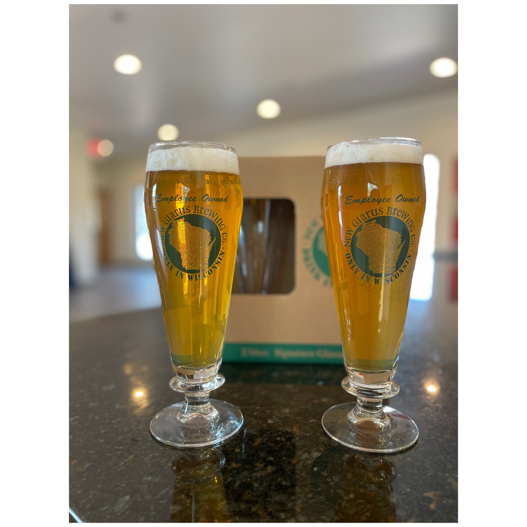 Two footed pilsner glasses with New Glarus Brewing Co, Only In Wisconsin circle logo on the front.